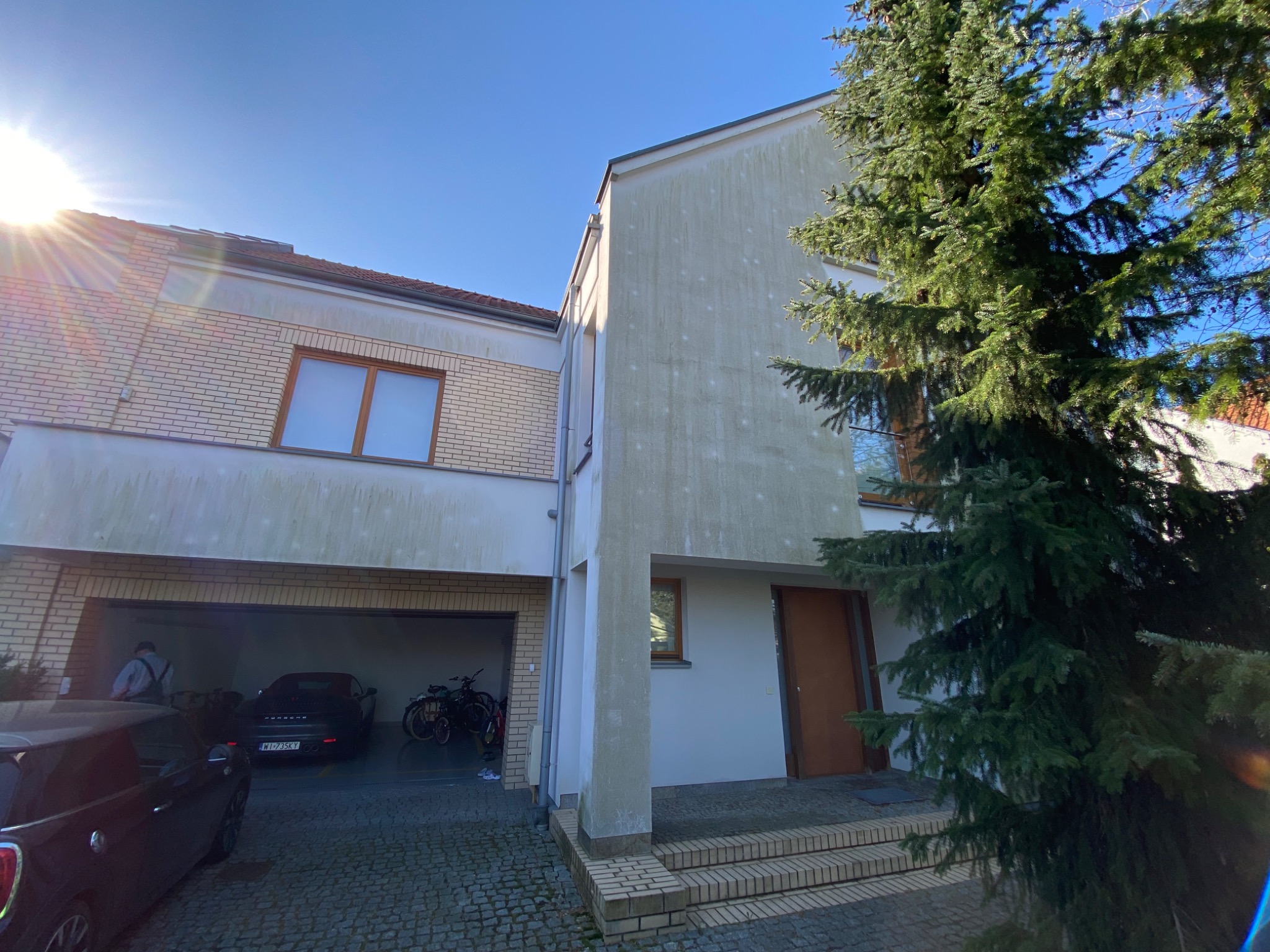 Dwukondygnacyjny dom jednorodzinny z garażem w bryle, widoczne ślady zabrudzeń na elewacji, kostka brukowa na podjeździe.