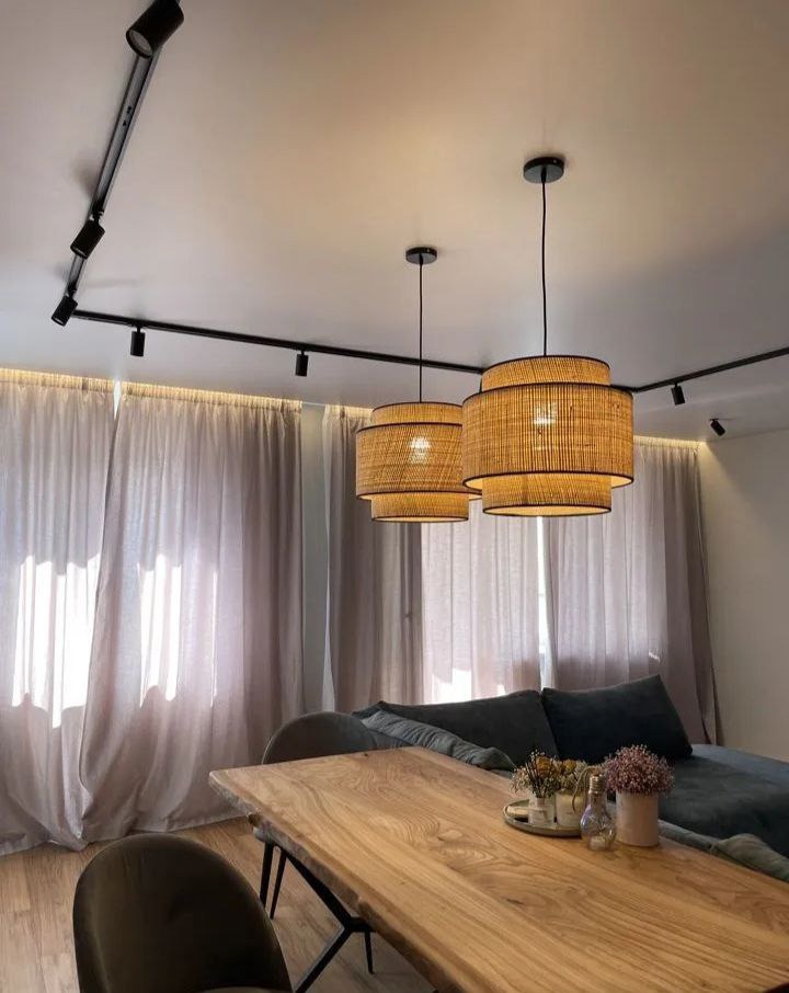 Nowoczesne wnętrze z drewnianym stołem, rattanowymi lampami wiszącymi i szynoprzewodem oświetleniowym na suficie.