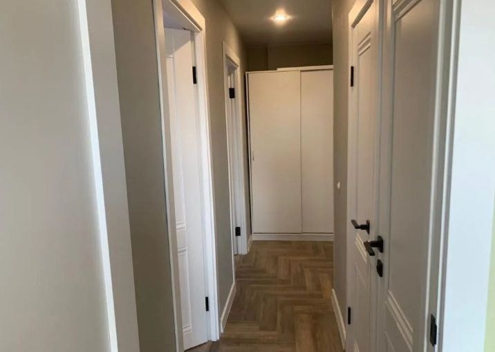 Korytarz po remoncie z parkietem w jodełkę, białymi drzwiami z czarnymi klamkami i szafą wnękową z przesuwnymi drzwiami.