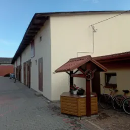 Elewacja budynku po tynkowaniu maszynowym, z dekoracyjną studnią i rowerami w tle, widok z brukowanego podwórka.