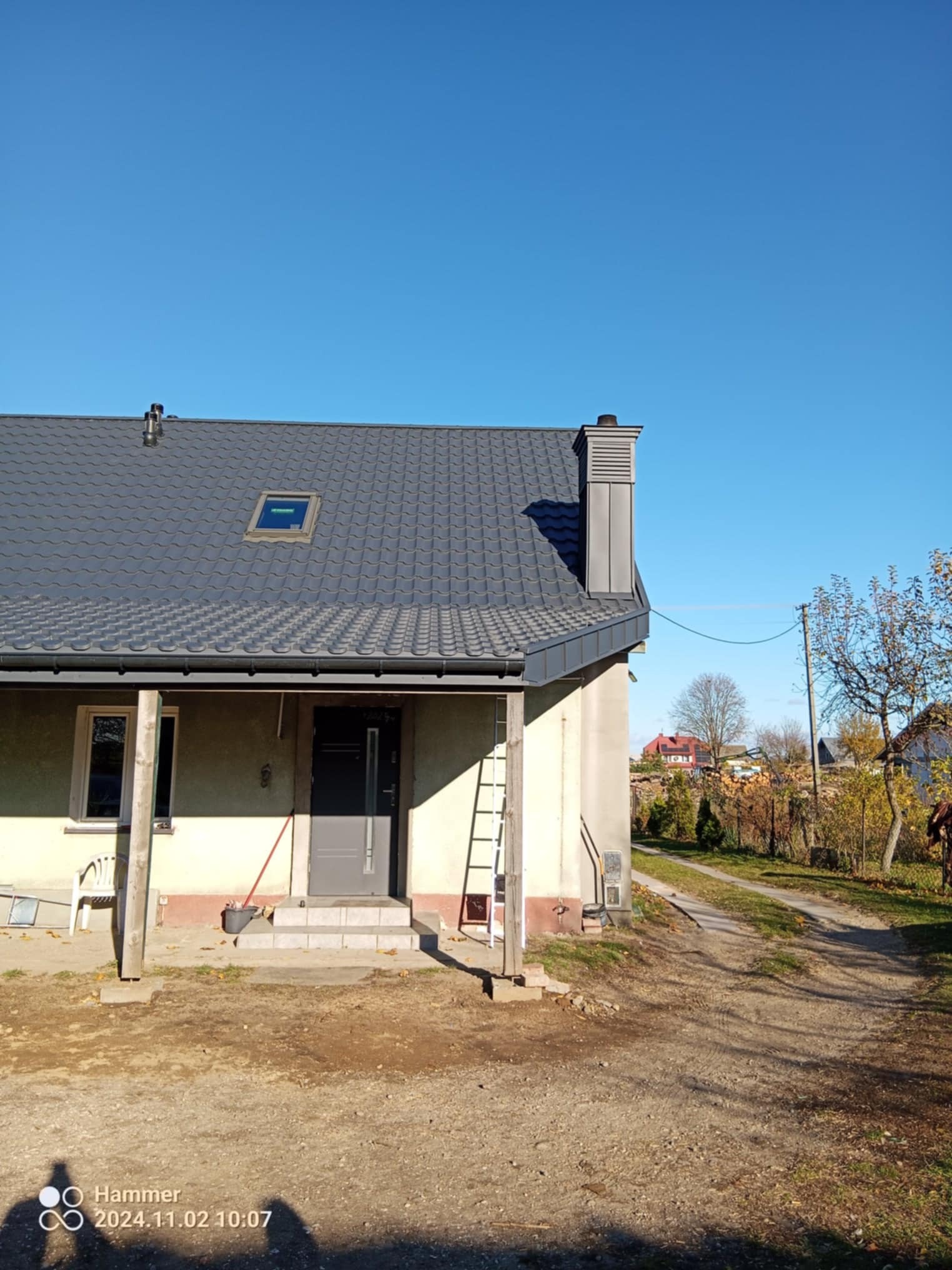 Dom jednorodzinny z nowym, grafitowym dachem z dachówki ceramicznej, widok z boku, drabina oparta o ścianę, błękitne niebo.