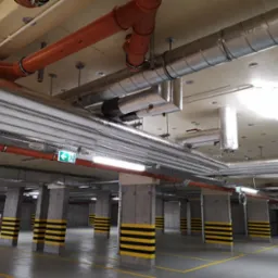 Instalacje wentylacyjne i rury w garażu podziemnym z betonowymi słupami pomalowanymi w czarno-żółte pasy.
