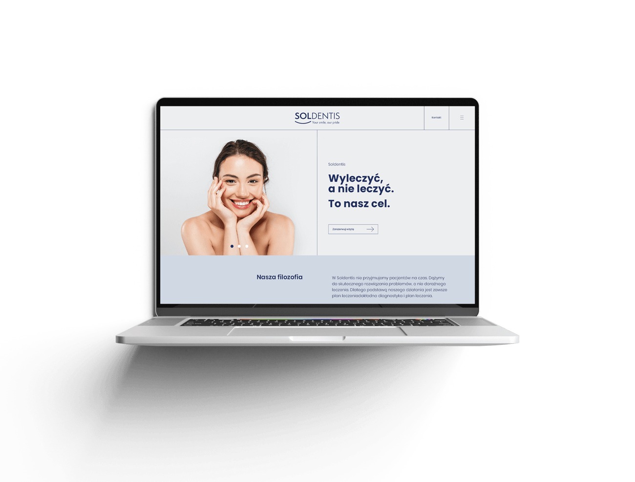 Laptop wyświetla minimalistyczny design strony internetowej dla gabinetu stomatologicznego Soldentis, z uśmiechniętą kobietą na banerze i hasłem 'Wyleczyć, a nie leczyć. To nasz cel.'