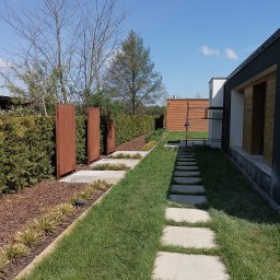 Mariusz Skora - Nowoczesny ogród z betonowymi płytami chodnikowymi w trawie, rustykalnymi panelami ogrodowymi i starannie przyciętym żywopłotem.