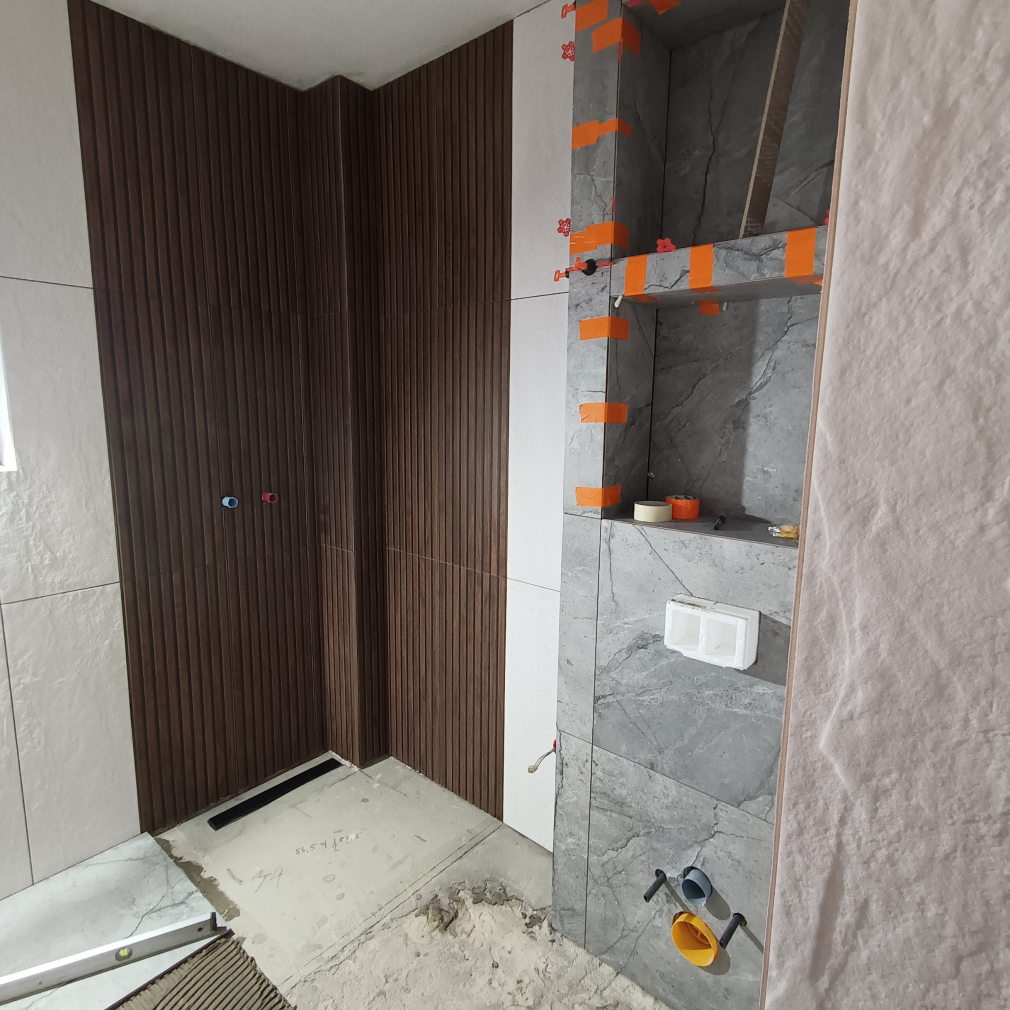 Łazienka w trakcie remontu w Piotrków Trybunalski: montaż płytek w strefie prysznicowej z wnęką, widoczne listwy dekoracyjne imitujące drewno na ścianie oraz poziomica na podłodze.