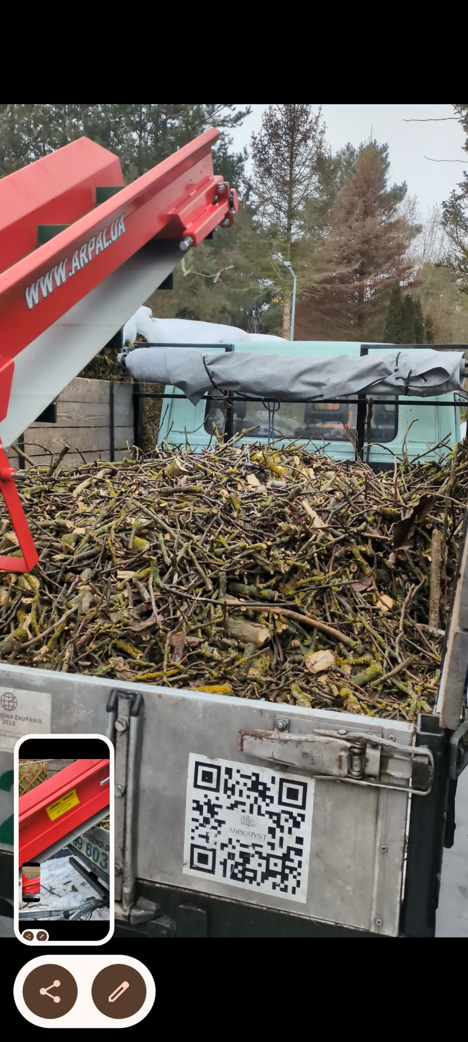 Ciężarówka wypełniona pociętymi gałęziami po wycince, z widocznym fragmentem rębaka z napisem 'www.arpal.ua' i naklejką z kodem QR firmy Arboryst.