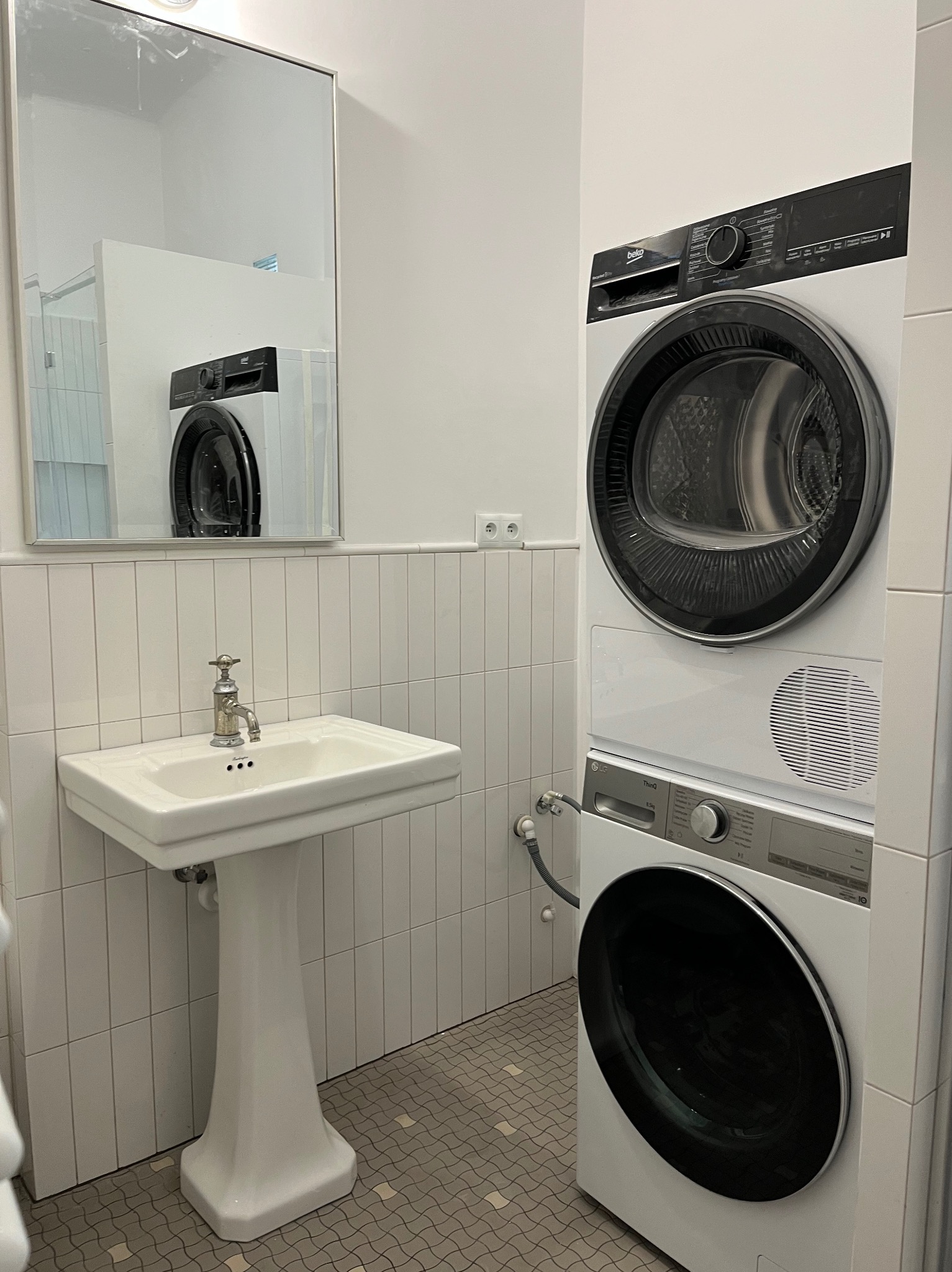 Biała łazienka z umywalką na postumencie i pralko-suszarką w zabudowie, widoczna w lustrze część kabiny prysznicowej.