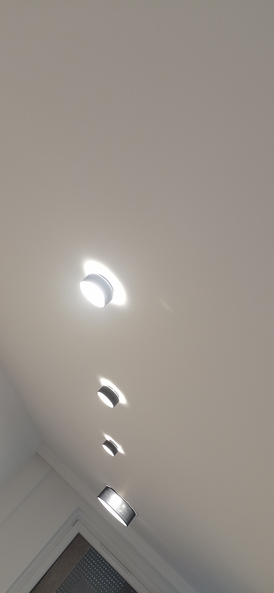 Rząd czterech okrągłych lamp sufitowych, od białej do czarnej, oświetlających biały sufit w nowym mieszkaniu, widok z dołu.