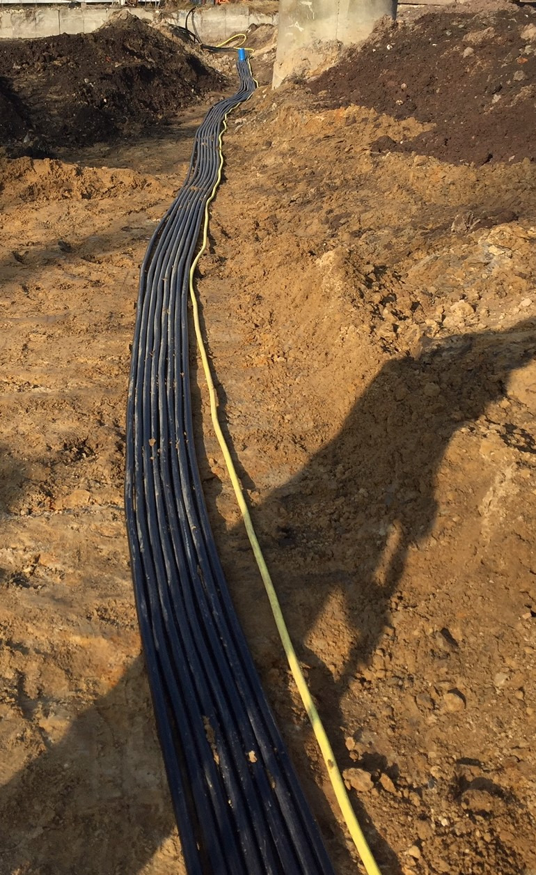 Wykop z ułożonymi rurami kablowymi w ziemi, widoczna żółta rura osłonowa, ziemia gliniasta.