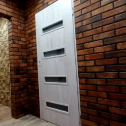 Wykończony korytarz z ceglaną ścianą, drewnopodobną podłogą i białymi drzwiami z przeszkleniami.