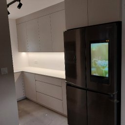 Studio Mebli Twoja Kuchnia.EU - Nowoczesna kuchnia z gładkimi, jasnymi frontami szafek i dużym, czarnym lodówko-zamrażarką Samsung z ekranem dotykowym wkomponowana w zabudowę.