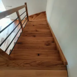 Spiralne schody drewniane z metalowymi balustradami, widok z dołu, naturalne oświetlenie, drewno z widocznymi słojami.