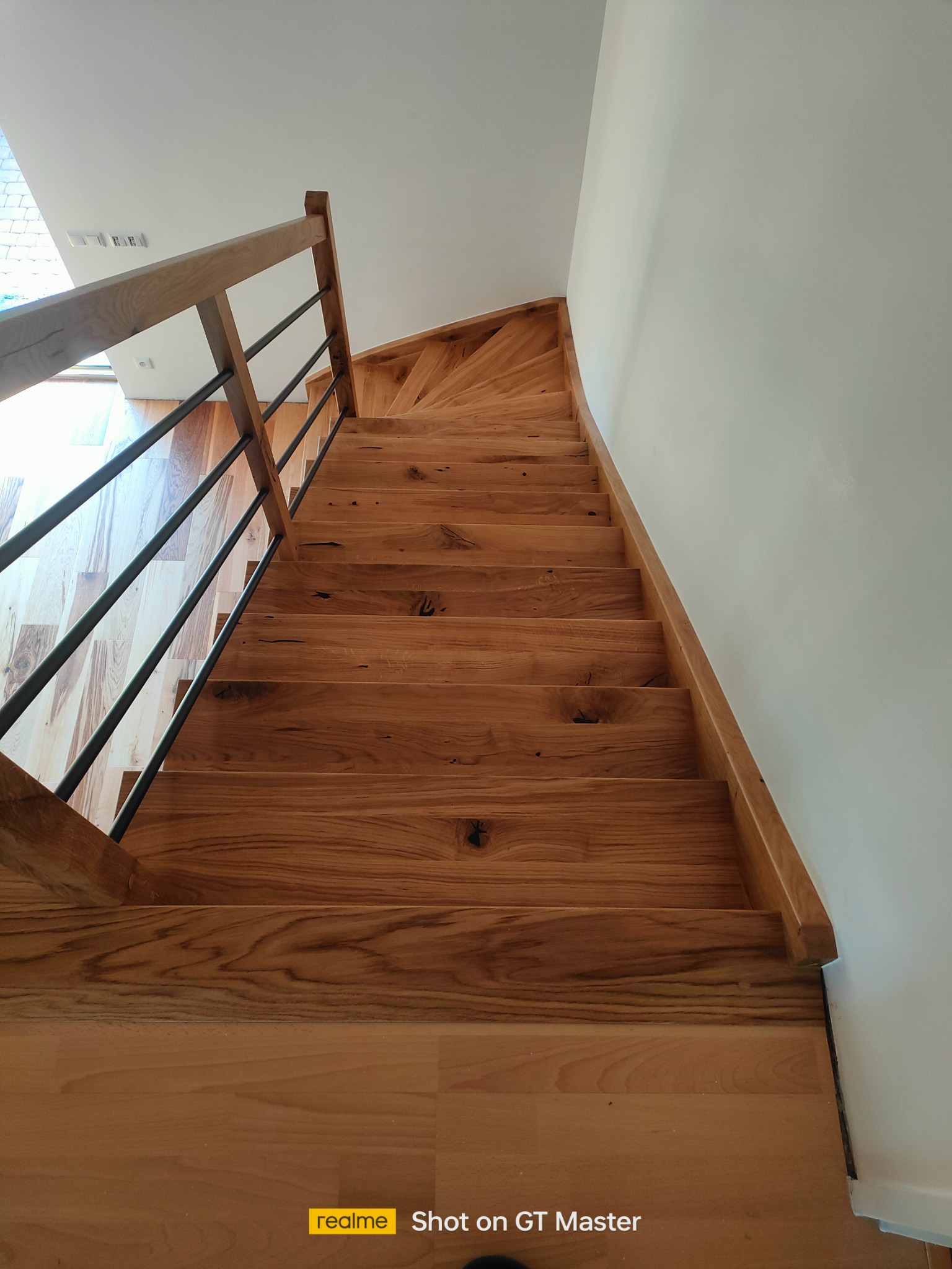 Spiralne schody drewniane z metalowymi balustradami, widok z dołu, naturalne oświetlenie, drewno z widocznymi słojami.