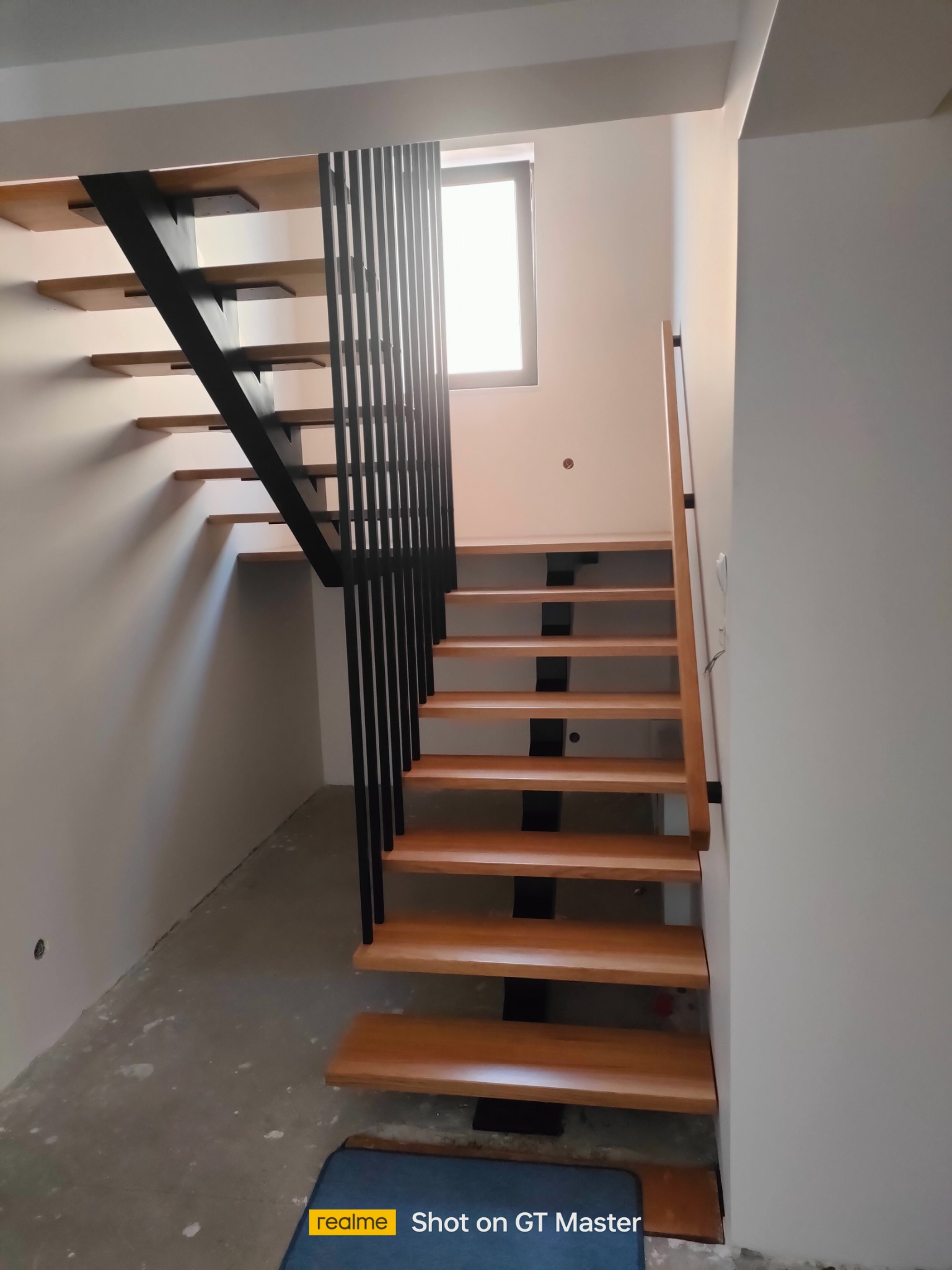 Nowoczesne schody z drewnianymi stopniami i metalową balustradą w minimalistycznym wnętrzu, widok z dołu na górę.