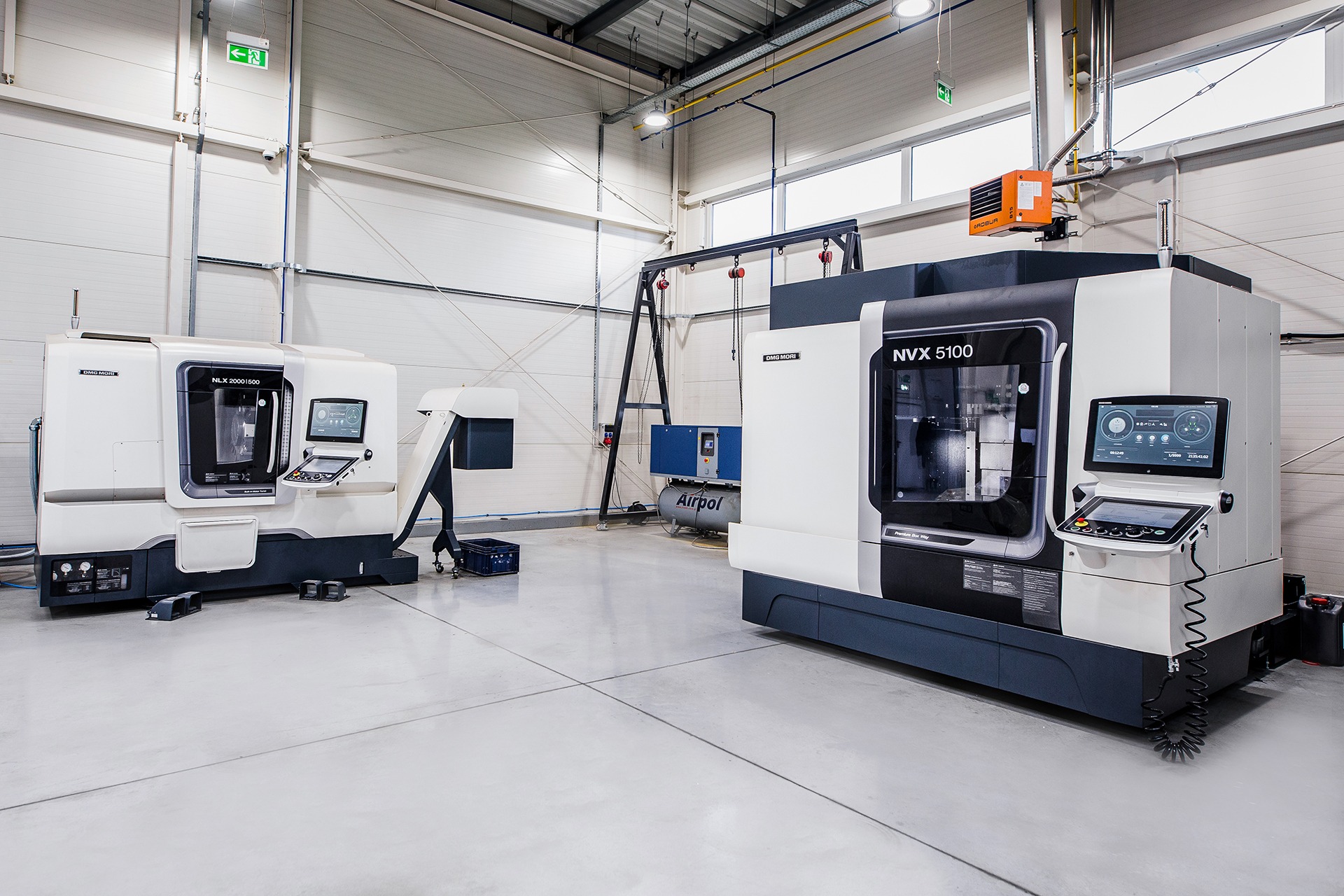 Dwie nowoczesne frezarki CNC DMG MORI (modele NLX 2000|500 i NVX 5100) w sterylnych warunkach hali produkcyjnej z widocznym oprzyrządowaniem i sterowaniem numerycznym.