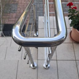 ZAPAŁA SŁAWOMIR - Polerowana balustrada nierdzewna na zewnątrz budynku, z kwiatami w doniczce w tle. Widok z góry, podkreślający detale wykończenia.