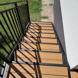 ZAPAŁA SŁAWOMIR - Schody zewnętrzne z metalową balustradą i drewnopodobnymi stopniami w jasnym otoczeniu. Widok z góry podkreśla geometrię konstrukcji i cień balustrady.