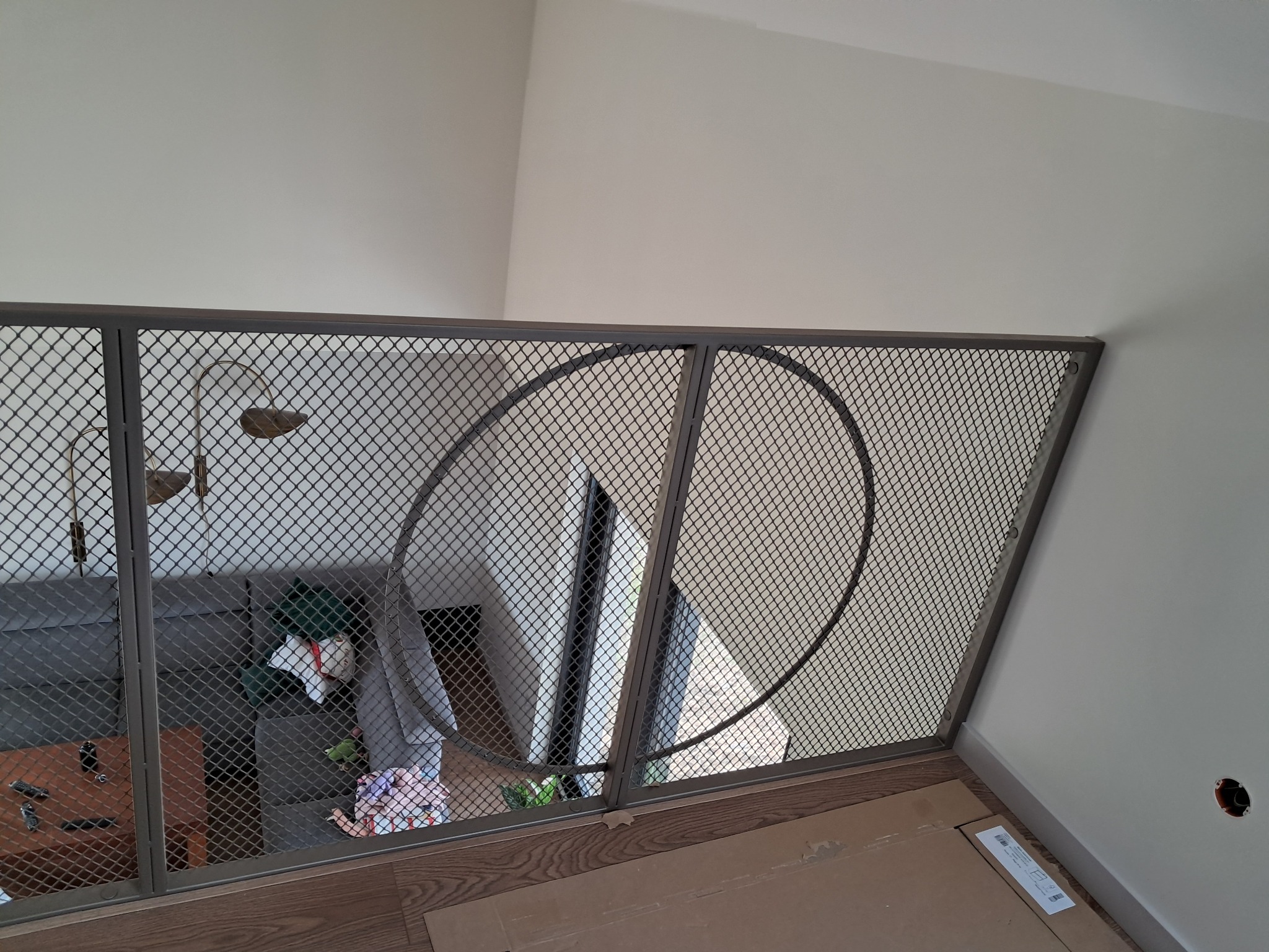 Metalowa balustrada z siatki z dekoracyjnymi okręgami na antresoli w nowoczesnym wnętrzu, widok z góry na salon z sofą i stolikiem.