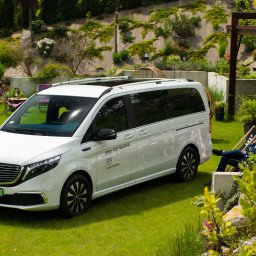 Tryb Manualny by Jakub Szołdra-Laszczyk - Biały Mercedes-Benz EQV z napisem Inter-Car Silesia na tle zielonego ogrodu z wypoczywającymi osobami w tle.