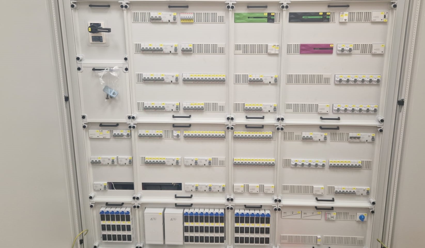 Rozbudowana, biała szafa elektryczna z licznymi zabezpieczeniami różnicowoprądowymi i modułami, widoczne akcesoria montażowe w woreczku i główny wyłącznik prądu.