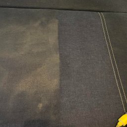 Czysty Sen pranie tapicerki w Lublinie - Fragment ciemnej tapicerki kanapy, widoczny efekt czyszczenia: lewa strona jaśniejsza, prawa strona ciemniejsza, z żółtą końcówką węża do prania w prawym dolnym rogu.