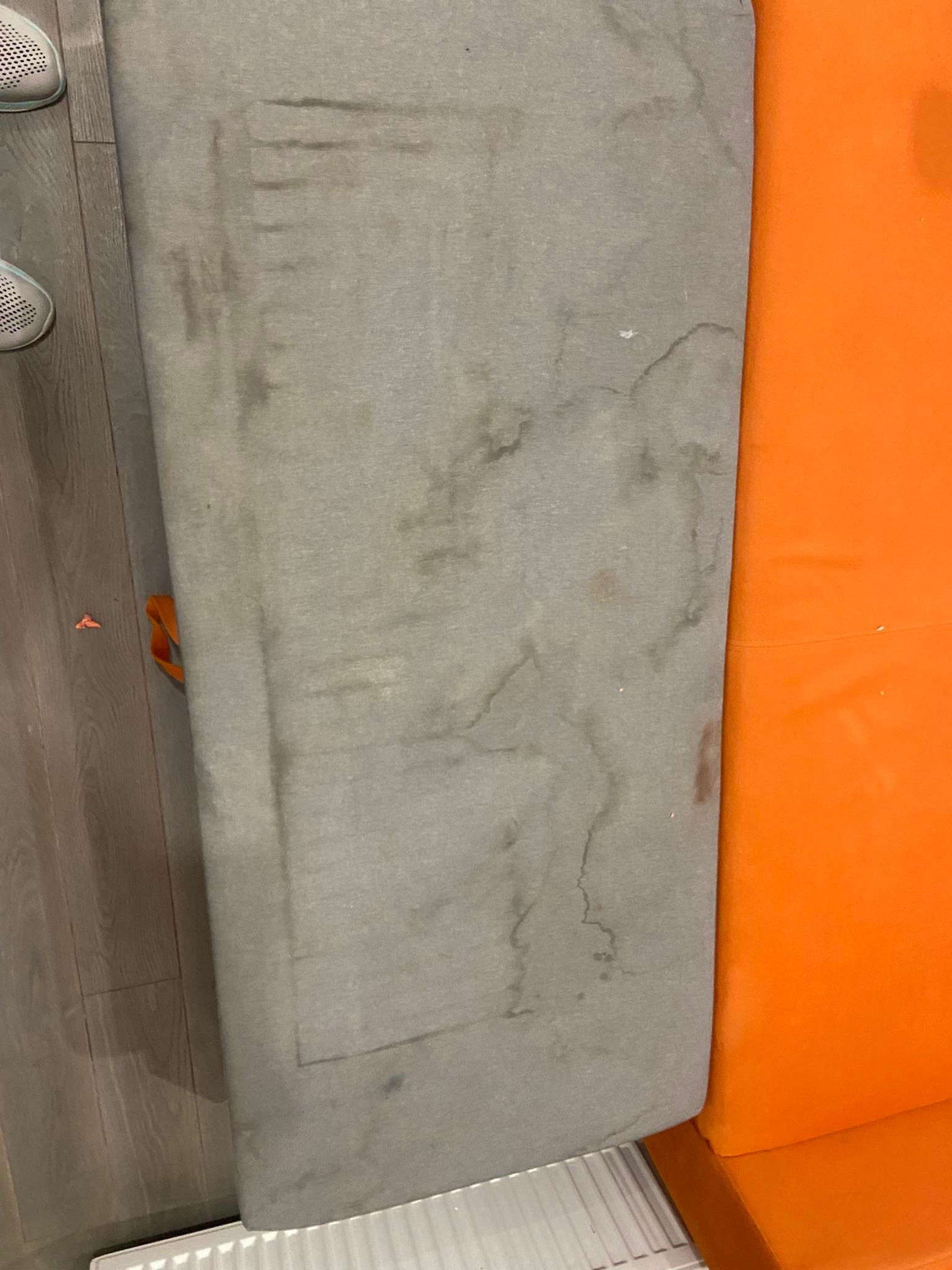 Szary, zabrudzony bok kanapy obok pomarańczowego boku, na podłodze z paneli.