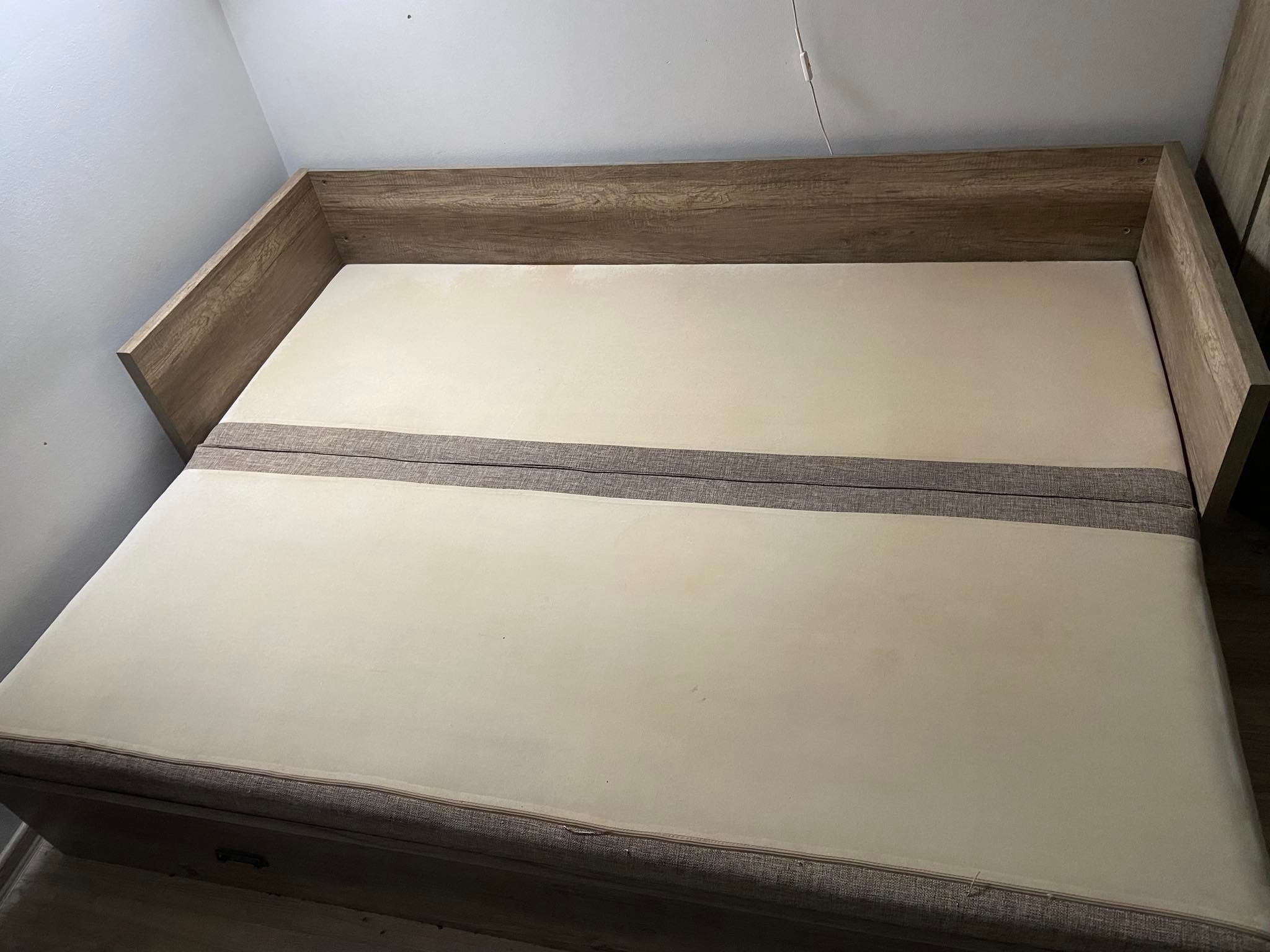 Materac na drewnianej ramie łóżka z szarą listwą dekoracyjną, widoczne plamy na powierzchni materaca.