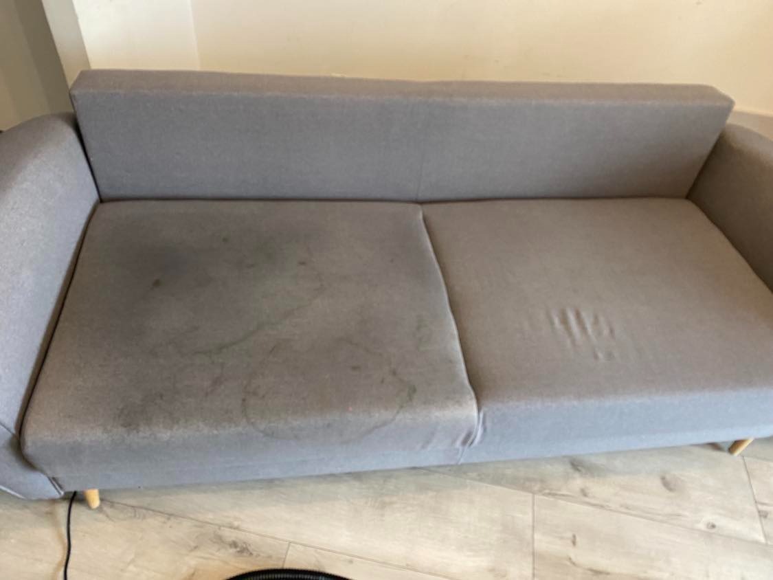 Szara, dwuosobowa kanapa z wyraźnymi plamami na jednym z siedzisk, widoczna różnica po czyszczeniu tapicerki w Lublinie.