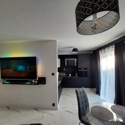 Łukasz Dyjas - Nowoczesne wnętrze z marmurową podłogą, czarną kuchnią w tle i telewizorem podświetlonym kolorowym światłem na ścianie.