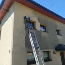 Malowanie elewacji domu jednorodzinnego z użyciem drabiny, widoczny fragment elewacji przed i po malowaniu, z numerem domu '23'.