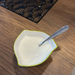 Ku zdrowiu - Porcja jogurtu naturalnego w miseczce z łyżeczką na drewnianym stole z czarną podkładką. Zdjęcie z góry, prezentacja zdrowego posiłku.