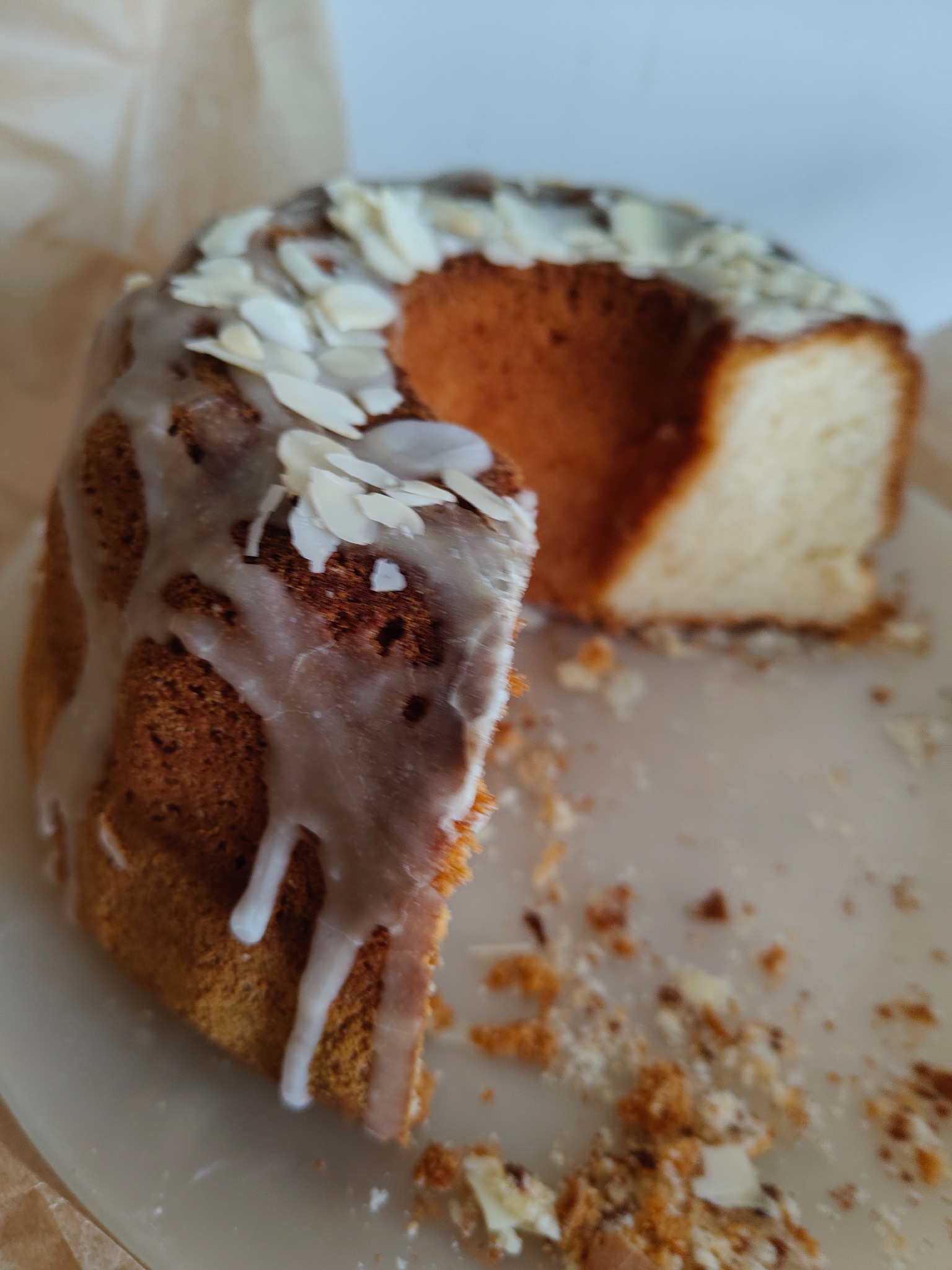 Kawałek babki drożdżowej z lukrem i płatkami migdałów na talerzu, z widocznymi okruchami.