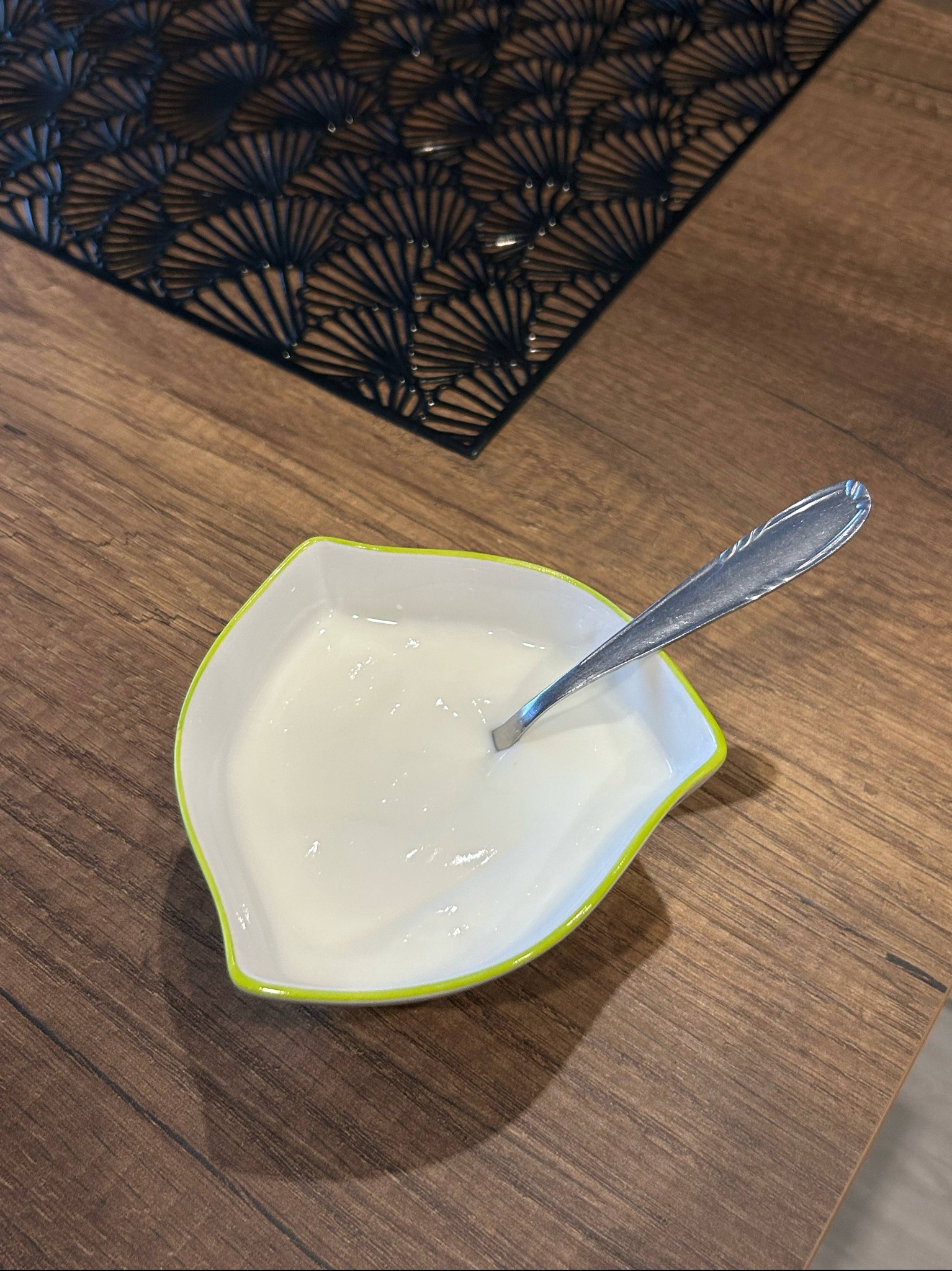 Porcja jogurtu naturalnego w miseczce z łyżeczką na drewnianym stole z czarną podkładką. Zdjęcie z góry, prezentacja zdrowego posiłku.