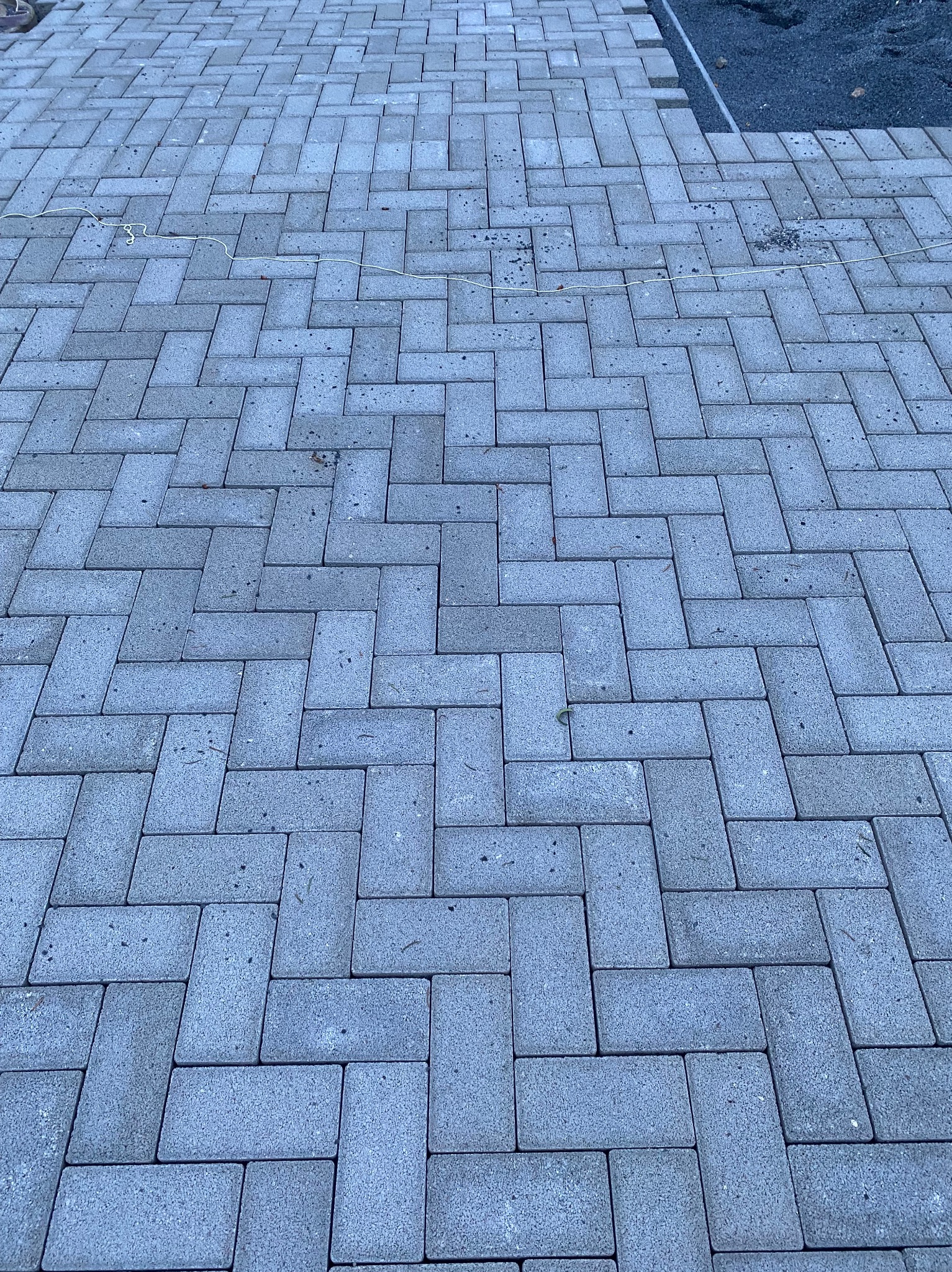 Ułożona szara kostka brukowa w jodełkę, widoczny fragment podsypki z boku.