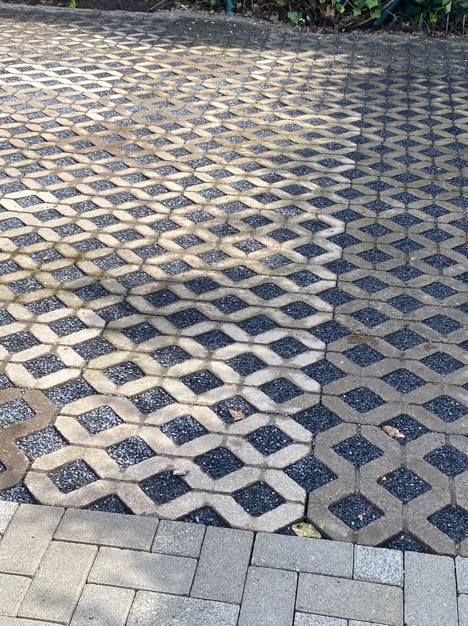 Szara ażurowa nawierzchnia z wypełnieniem z drobnego kamienia, fragment klasycznej kostki brukowej w dolnej części kadru.