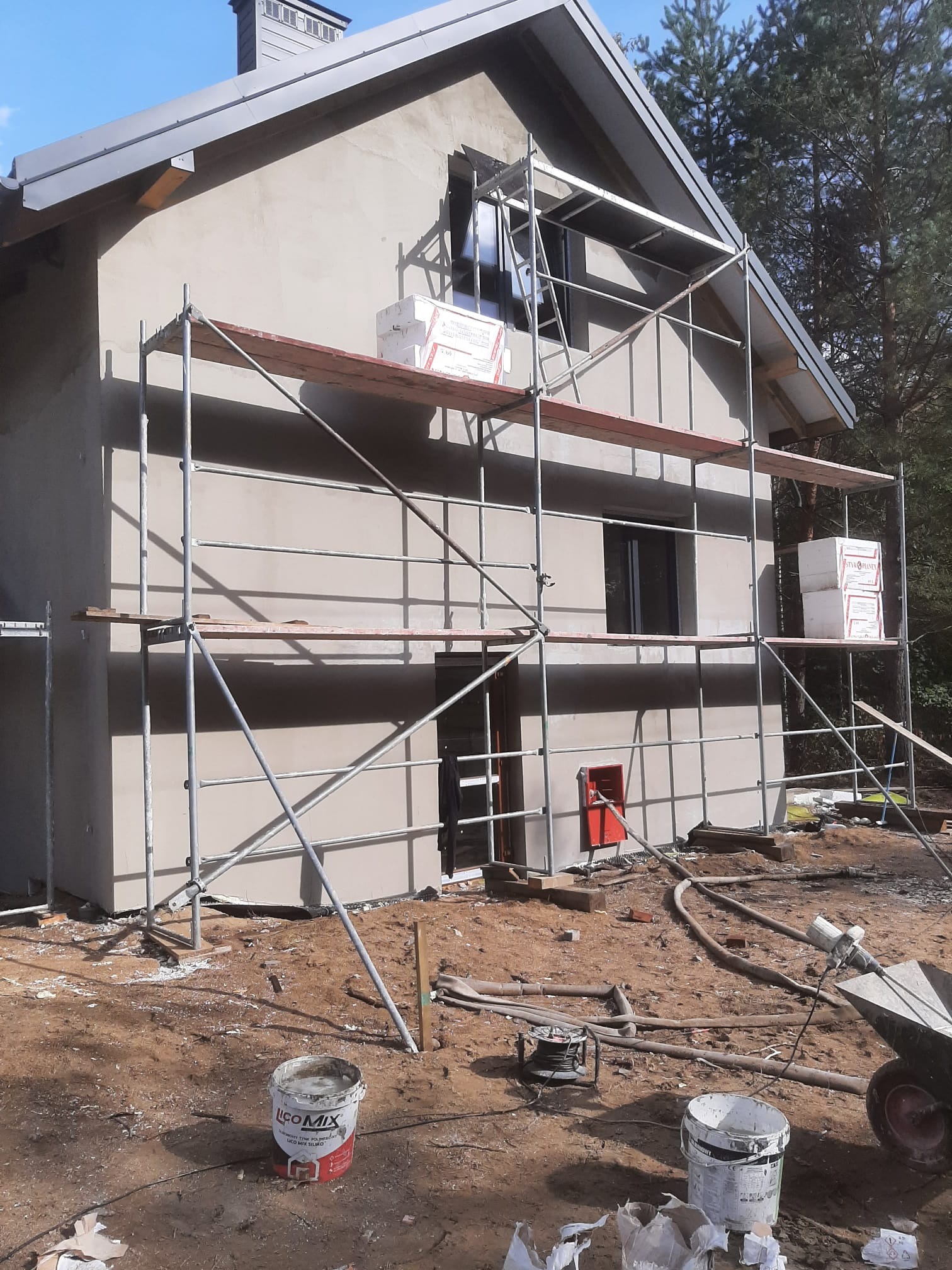 Dom w Zamościu w trakcie ocieplania, widoczne rusztowania, ściany pokryte szarym tynkiem, styropian na rusztowaniu, przygotowane wiadra z zaprawą.