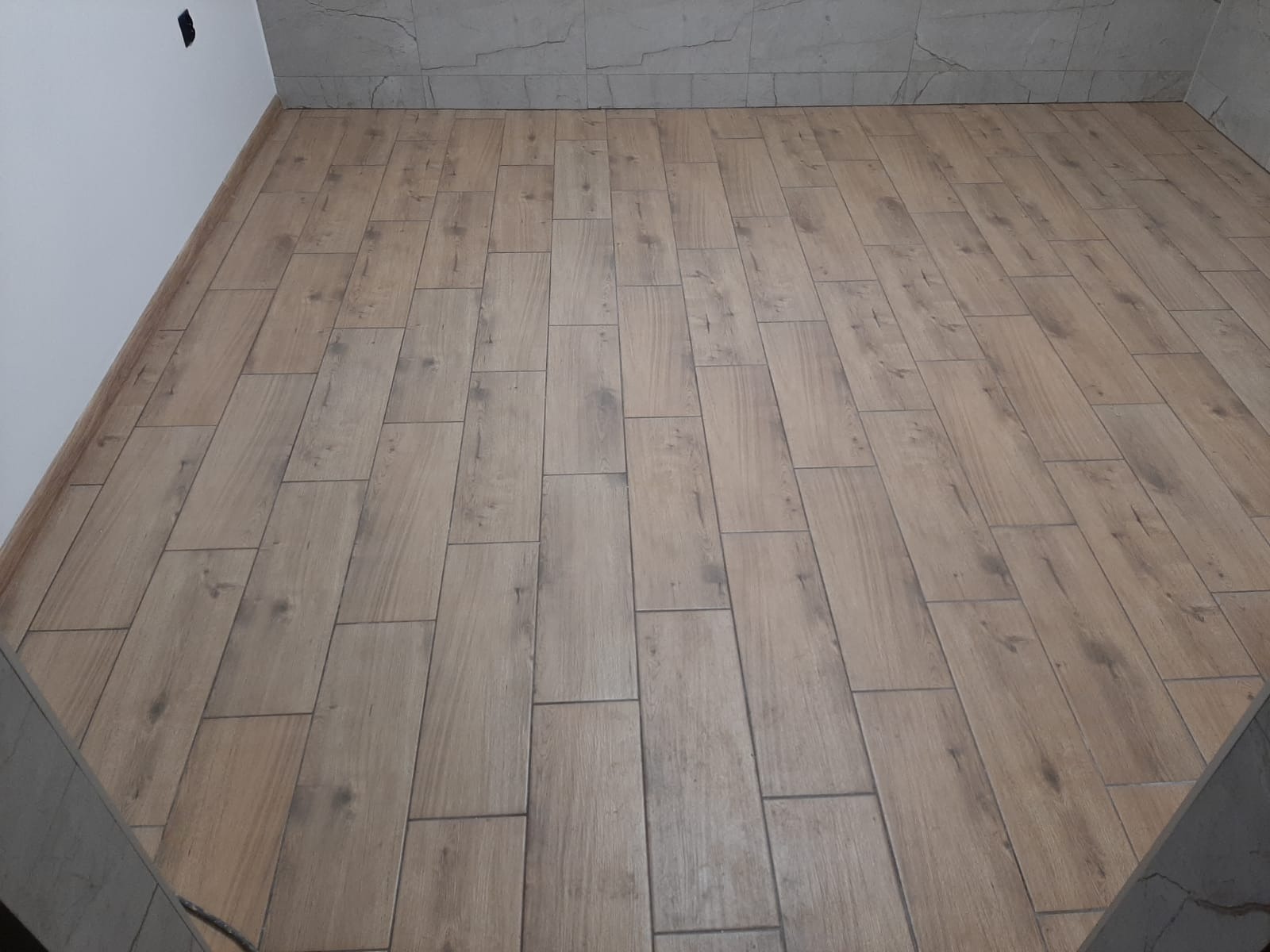 Ułożona podłoga z paneli imitujących drewno, widok z góry, ściany wykończone płytkami imitującymi marmur.