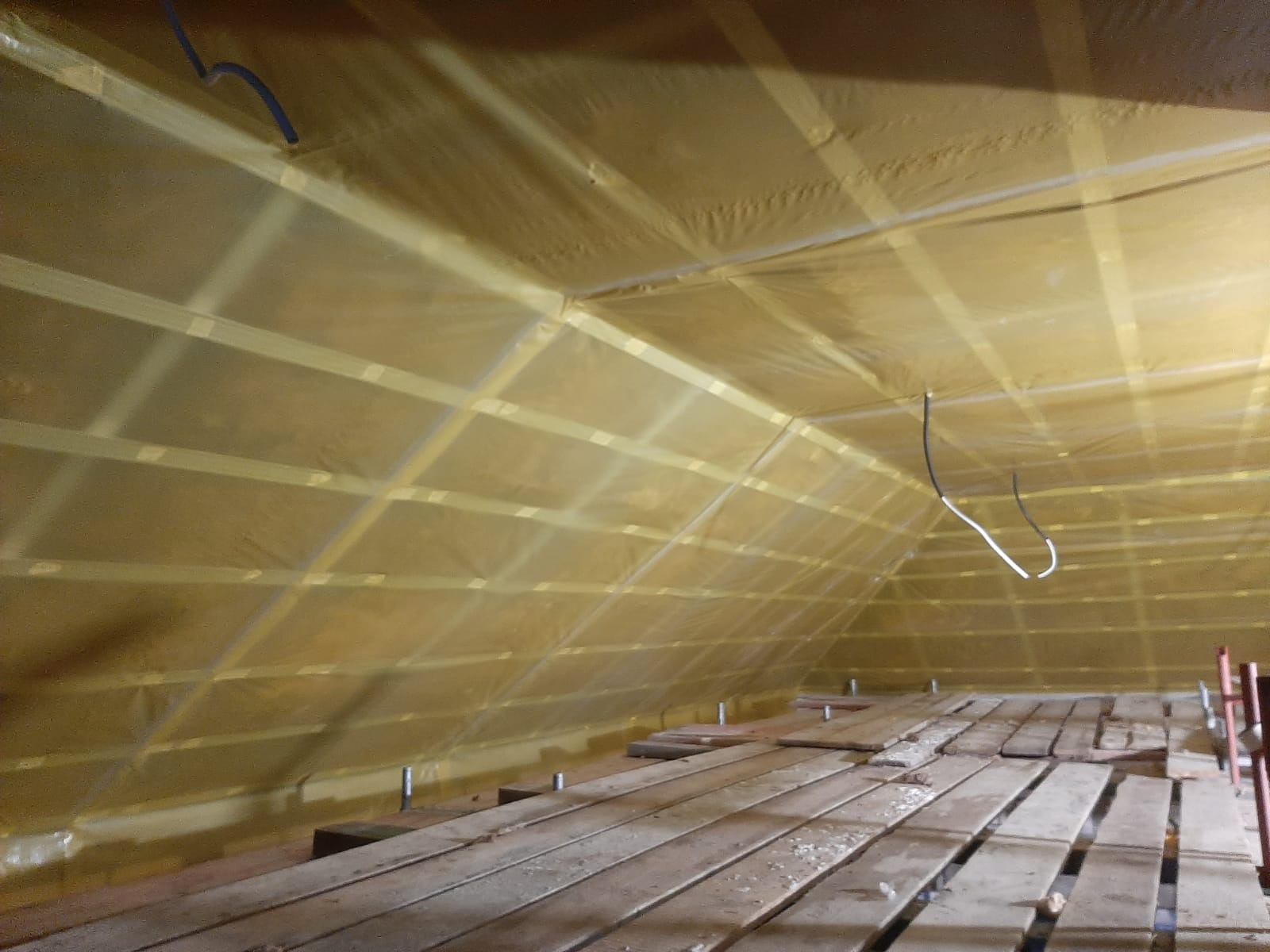 Poddasze w trakcie izolacji folią paroizolacyjną, widoczne drewniane belki konstrukcyjne i wystające kable elektryczne.