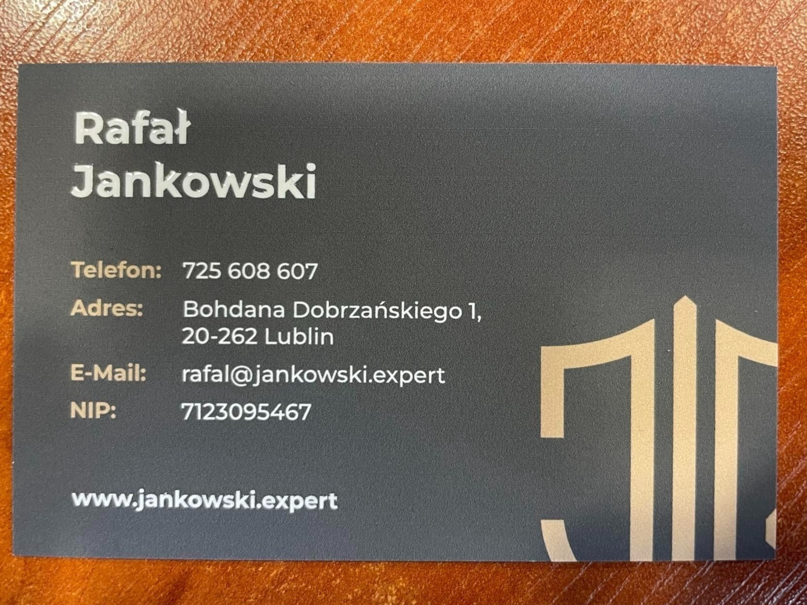 Wizytówka Rafała Jankowskiego z numerem telefonu, adresem, e-mailem i NIP-em, na ciemnoszarym tle z złotym logo po prawej stronie.