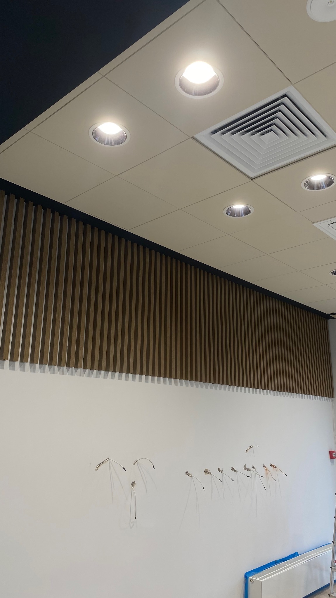 Montaż drewnianych paneli ściennych w biurze, widoczne wystające kable elektryczne i fragment sufitu z oświetleniem punktowym.