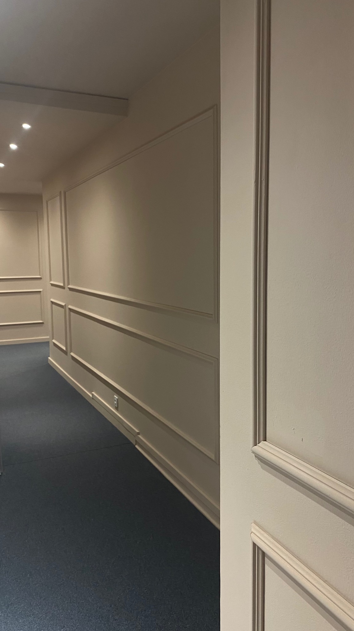 Korytarz z wykończonymi ścianami z płyt kartonowo-gipsowych z dekoracyjnymi listwami w kolorze kremowym i ciemną podłogą, widok z perspektywy.