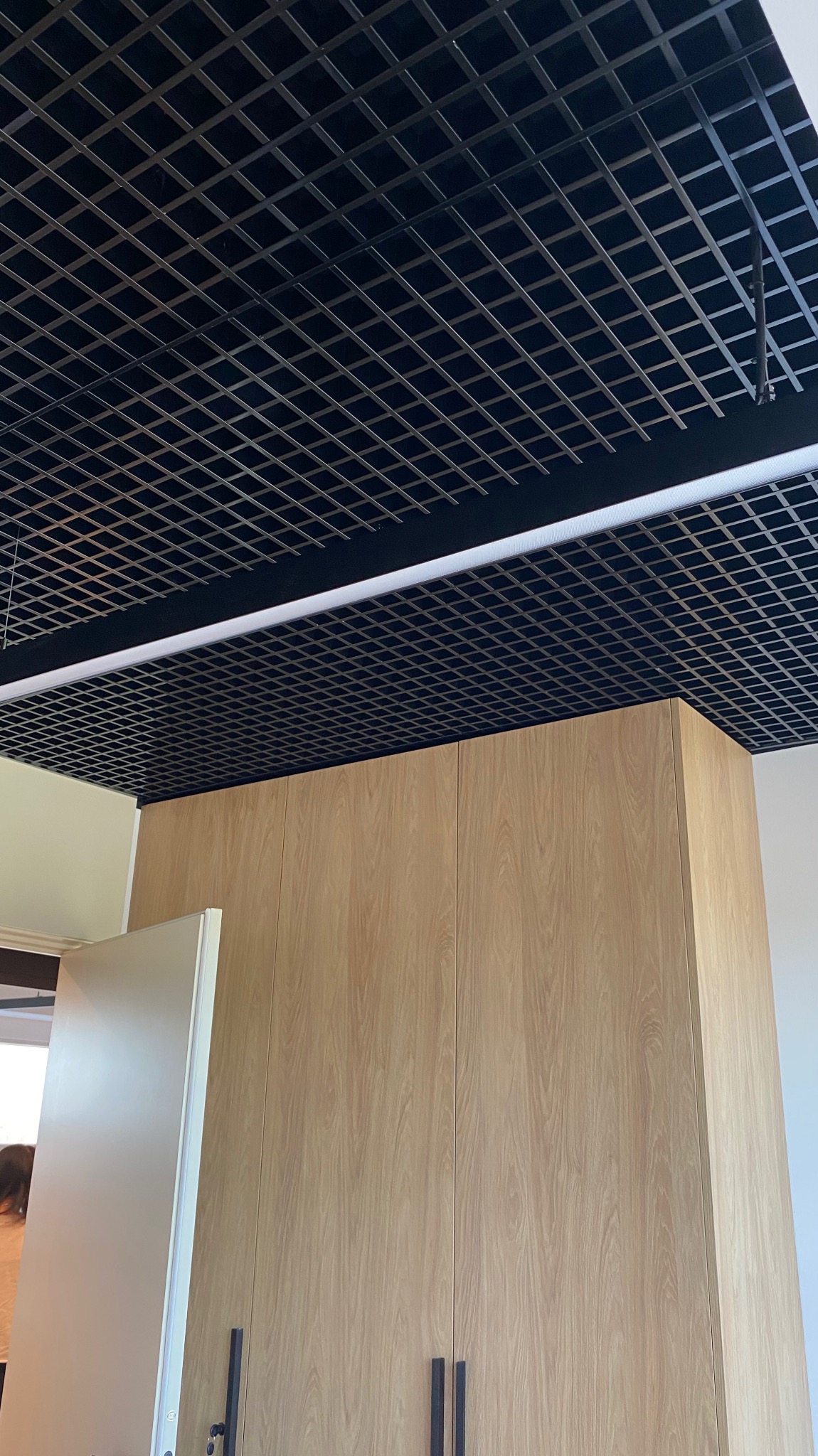 Czarny sufit rastrowy z oświetleniem liniowym nad szafą wnękową z drewnopodobnymi frontami, widoczne w mieszkaniu w Warszawie.