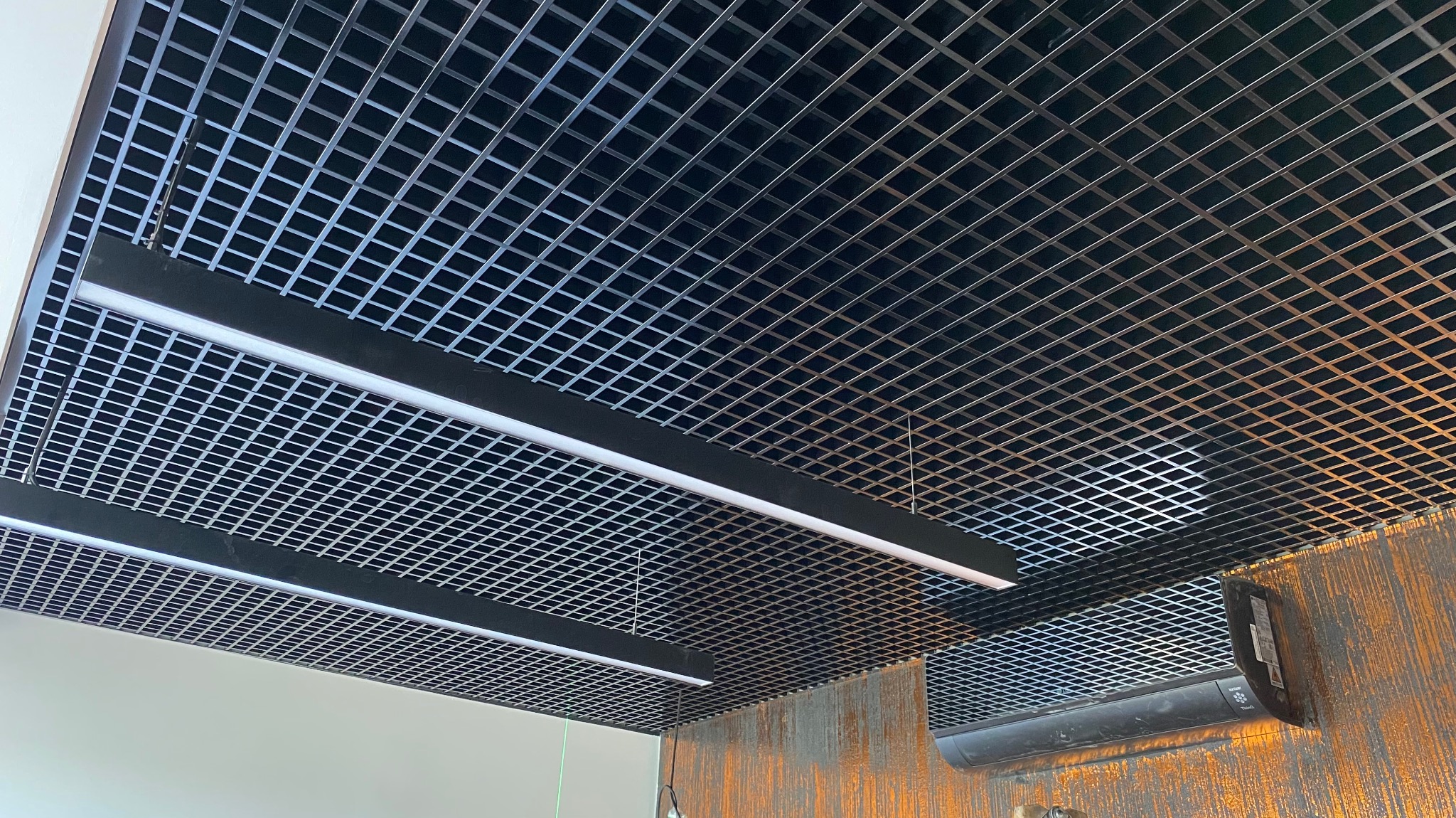 Sufit rastrowy z oświetleniem liniowym LED, widoczny klimatyzator na rustykalnej ścianie.