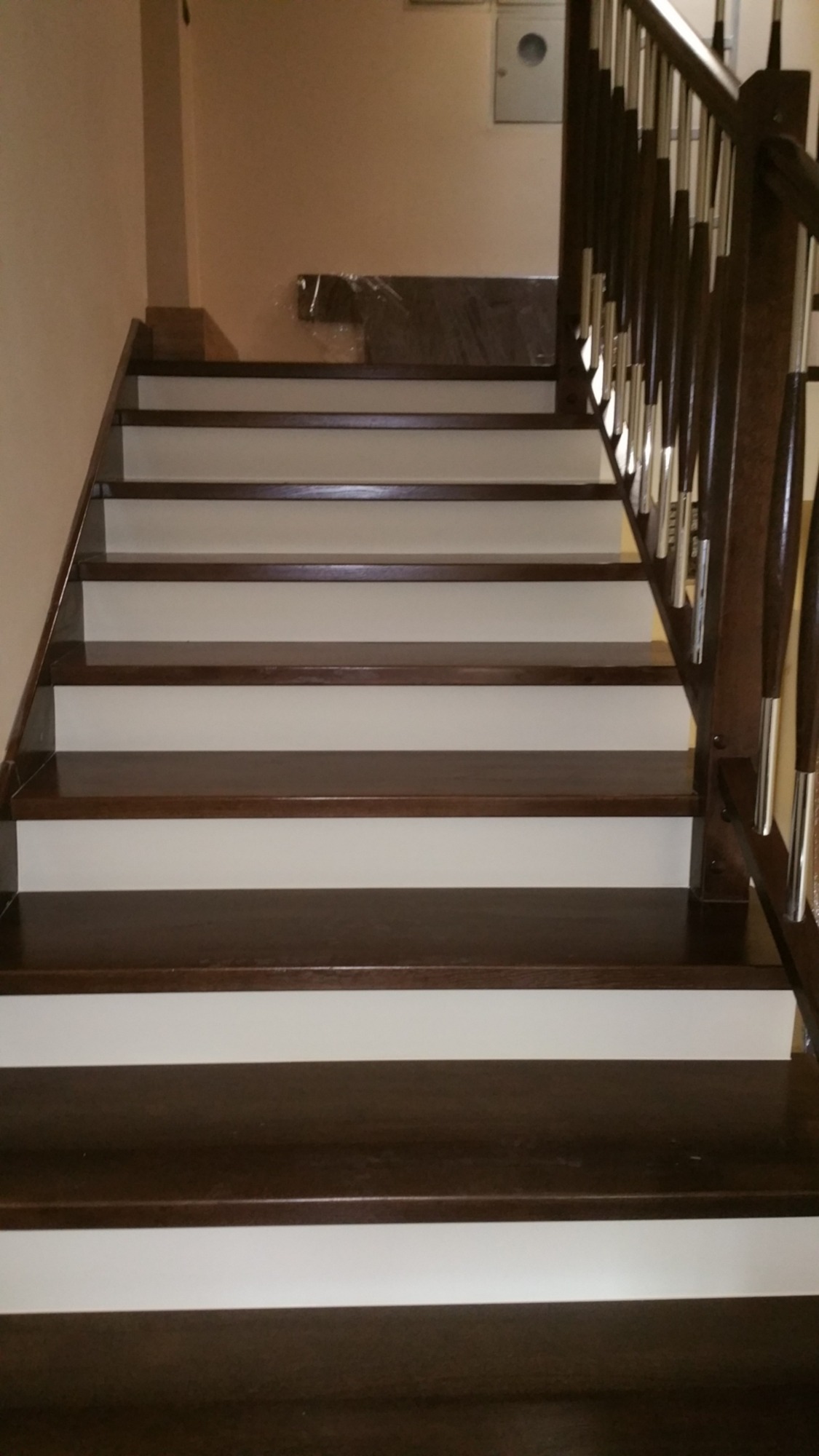 Bieg schodów z ciemnego drewna z białymi podstopnicami i balustradą z brązowego drewna oraz srebrnymi prętami.