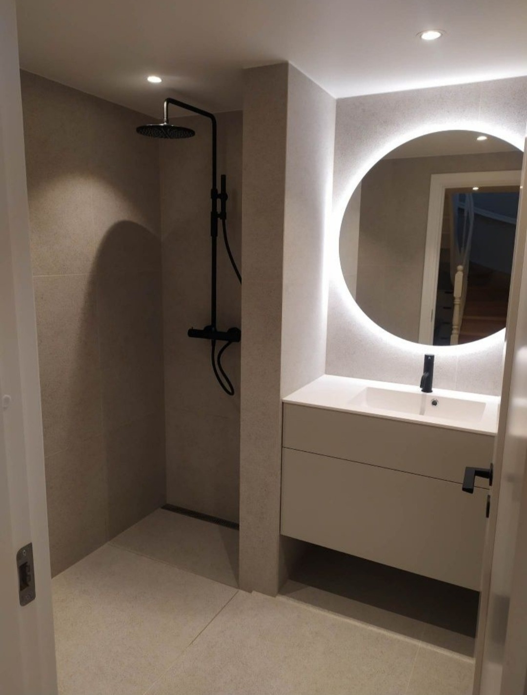 Nowoczesna łazienka z kabiną prysznicową typu walk-in z czarną armaturą, umywalką nablatową na szafce i okrągłym lustrem z podświetleniem LED.