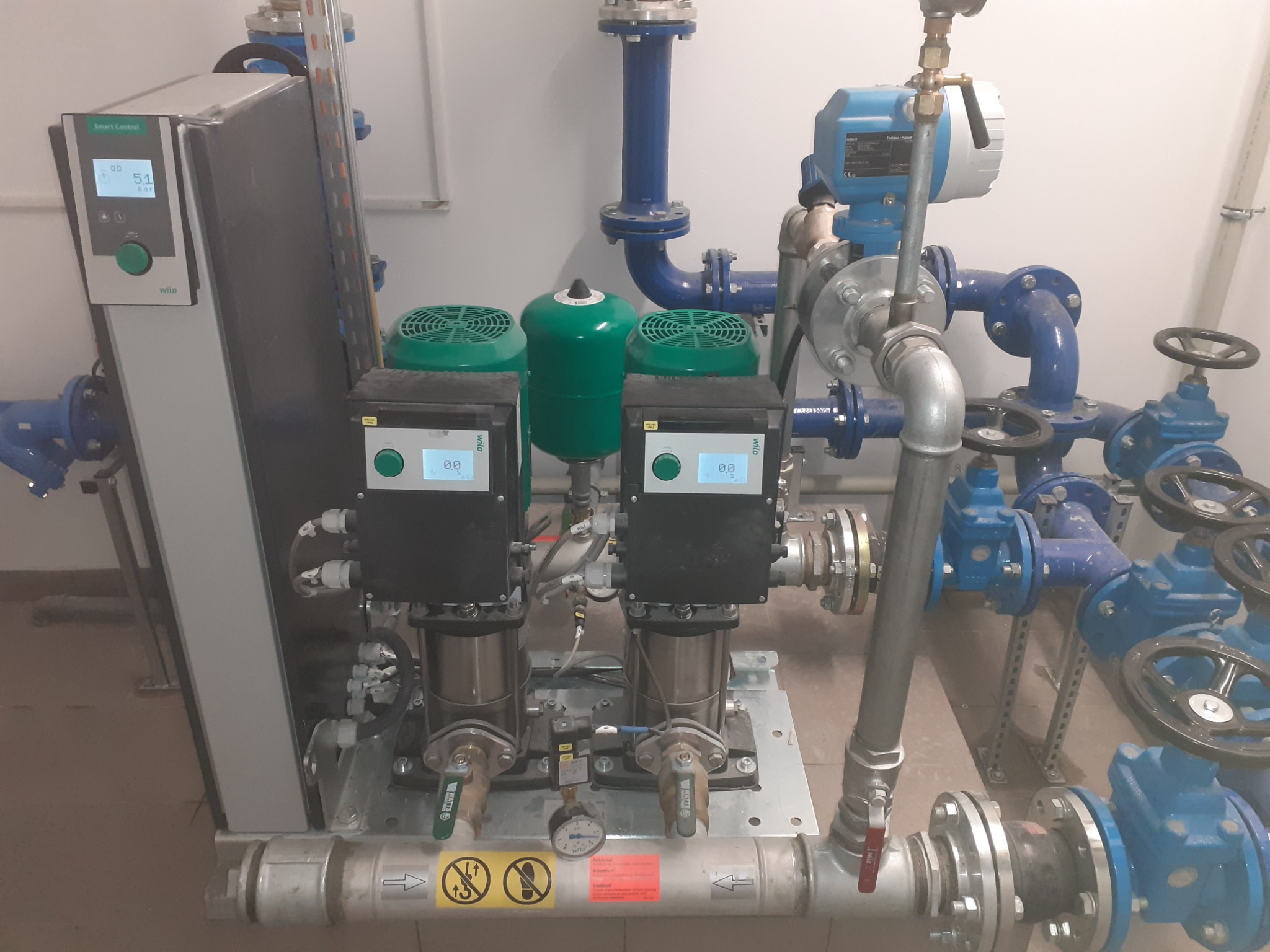 Kompleksowa instalacja pompowni hydroforowej Wilo z dwoma pompami, zbiornikiem przeponowym, armaturą i sterownikiem Smart Control, widoczne przyłącza wodne z zaworami.