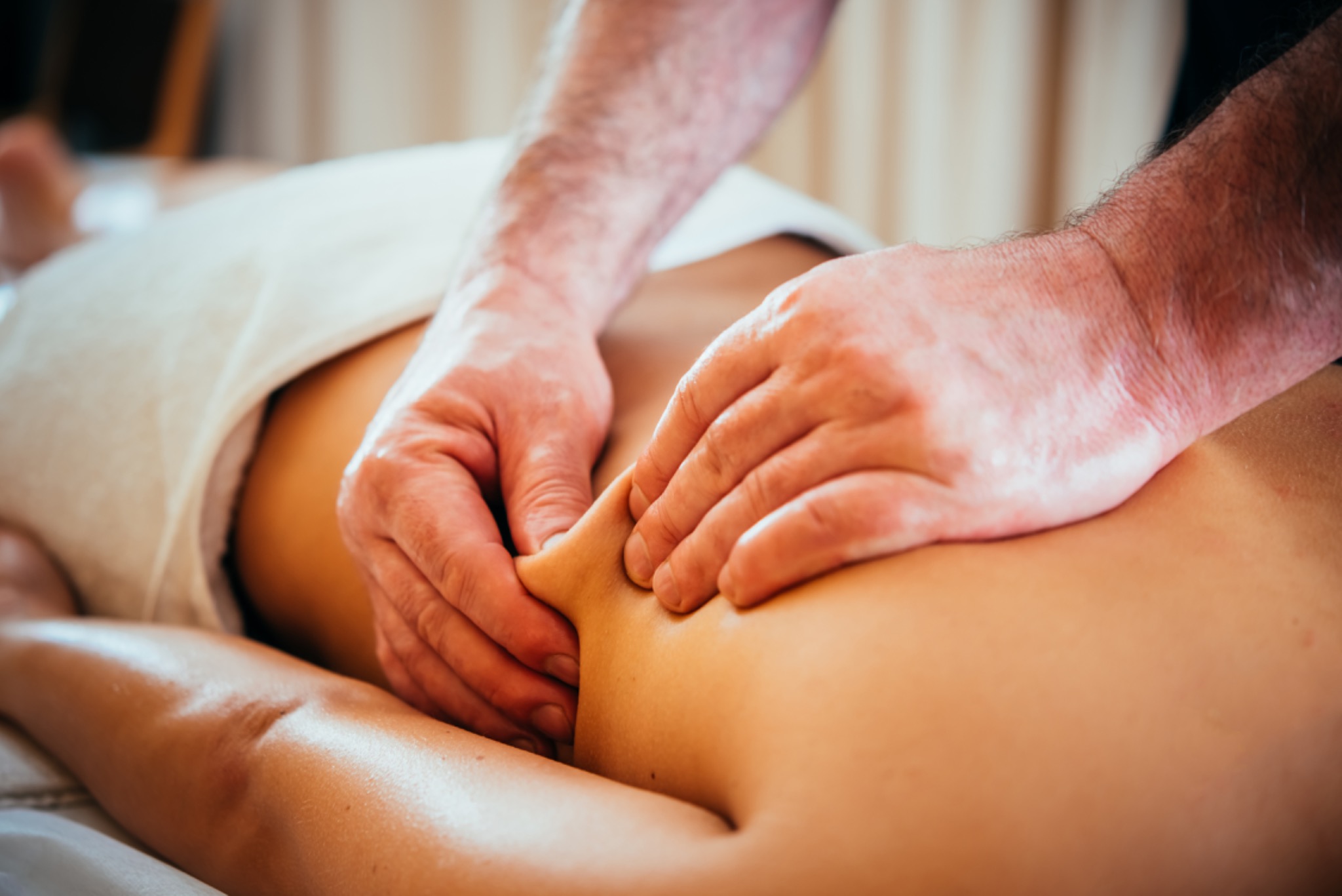 Masażysta ugniata mięśnie ramienia pacjenta leżącego na stole przykrytym białym ręcznikiem.