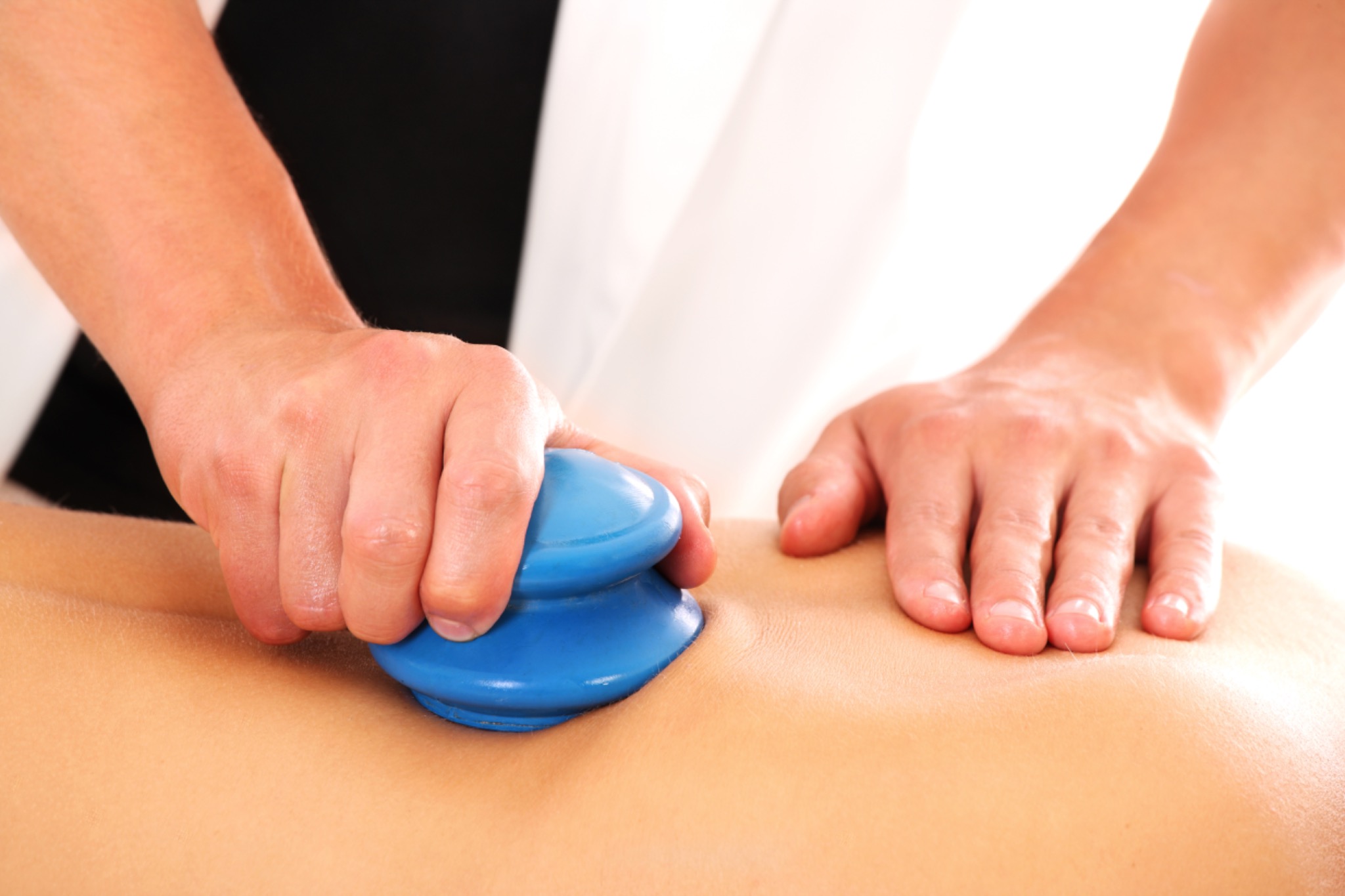 Masaż bańkami na plecach pacjenta wykonywany przez masażystę w białym uniformie.