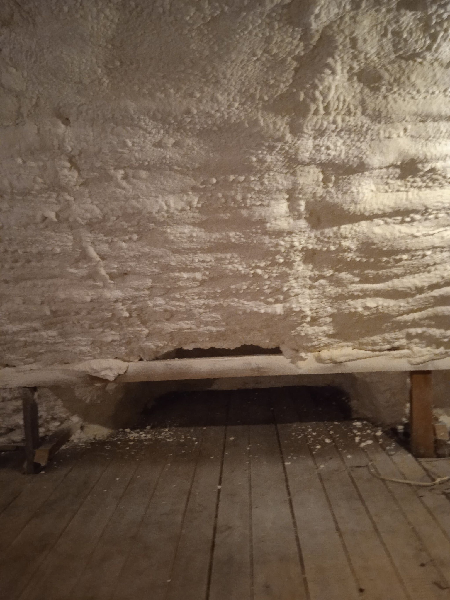 Poddasze z drewnianą podłogą i izolacją natryskową, widoczne nierówności i fragmenty pianki na podłodze.