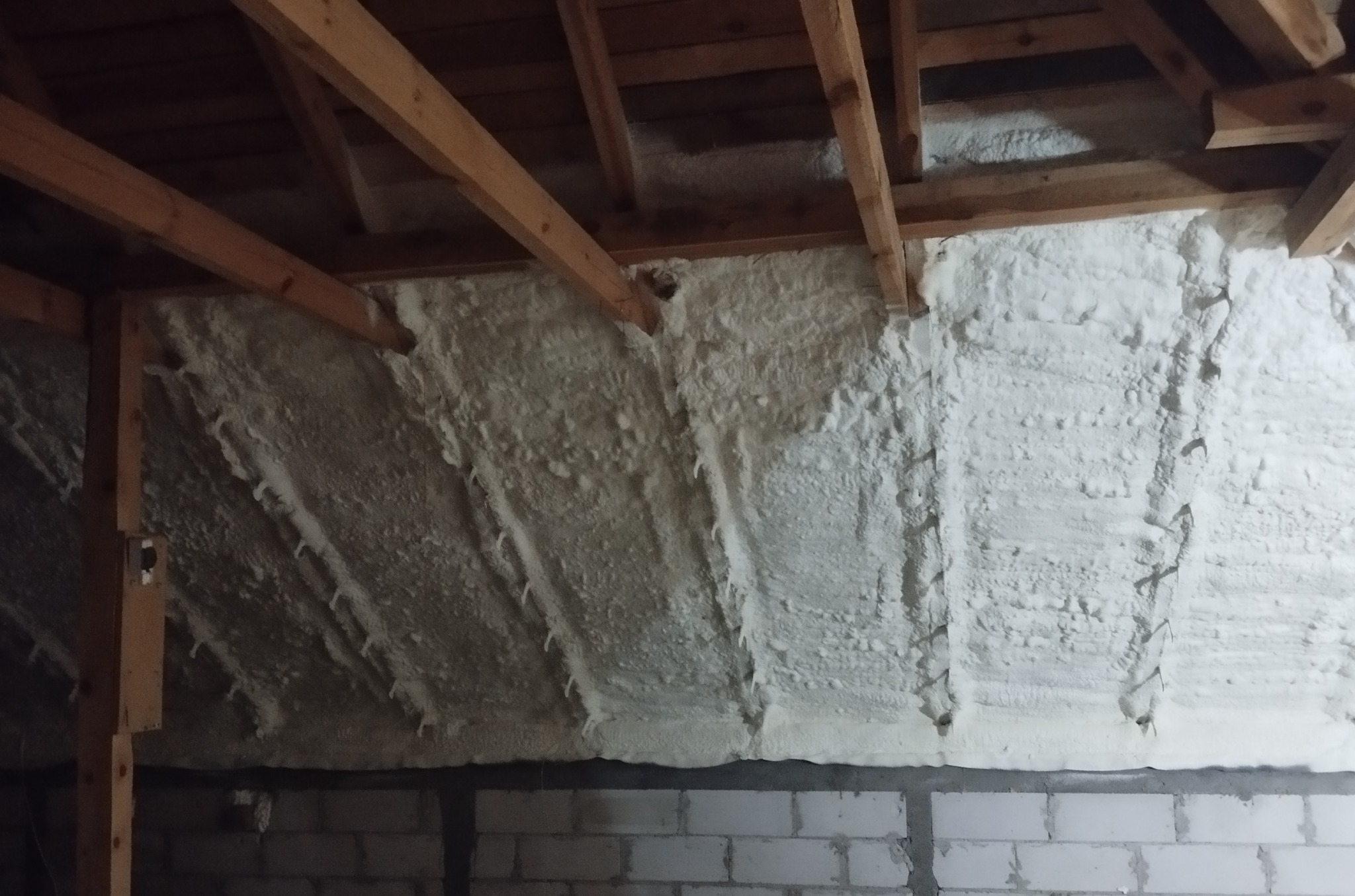 Poddasze z widoczną drewnianą konstrukcją dachu, pokryte grubą warstwą jasnej pianki izolacyjnej, na dole widoczne ściany z bloczków betonowych.